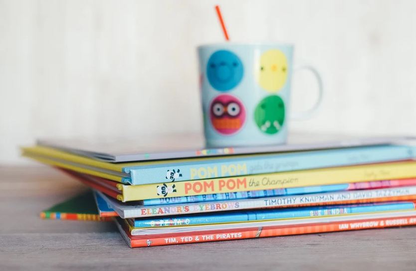 Children Books piled with a smiley-faced cup placed on it